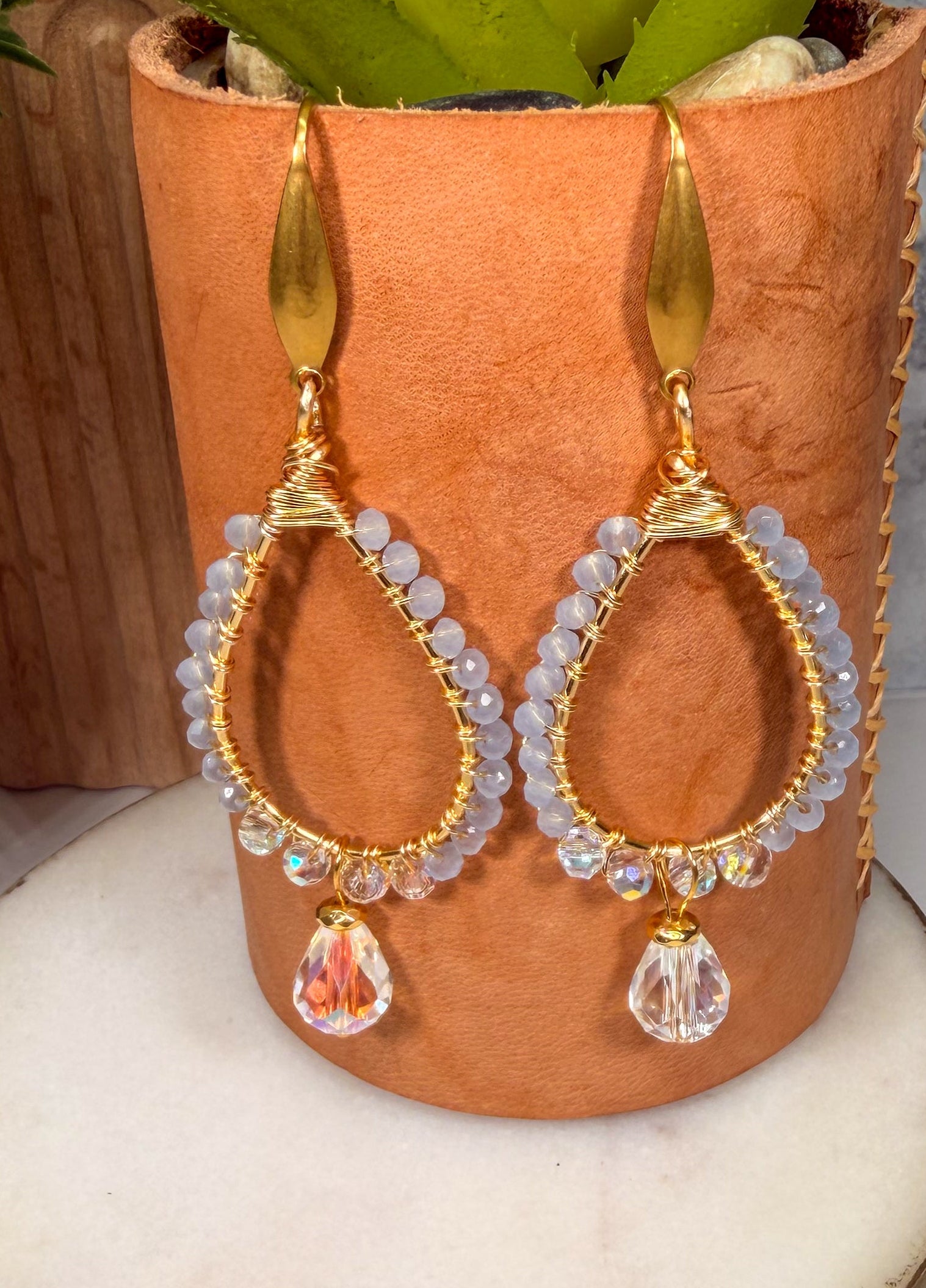 Gold hoop earrings with gemstones on a marble surface with a plant in the background
