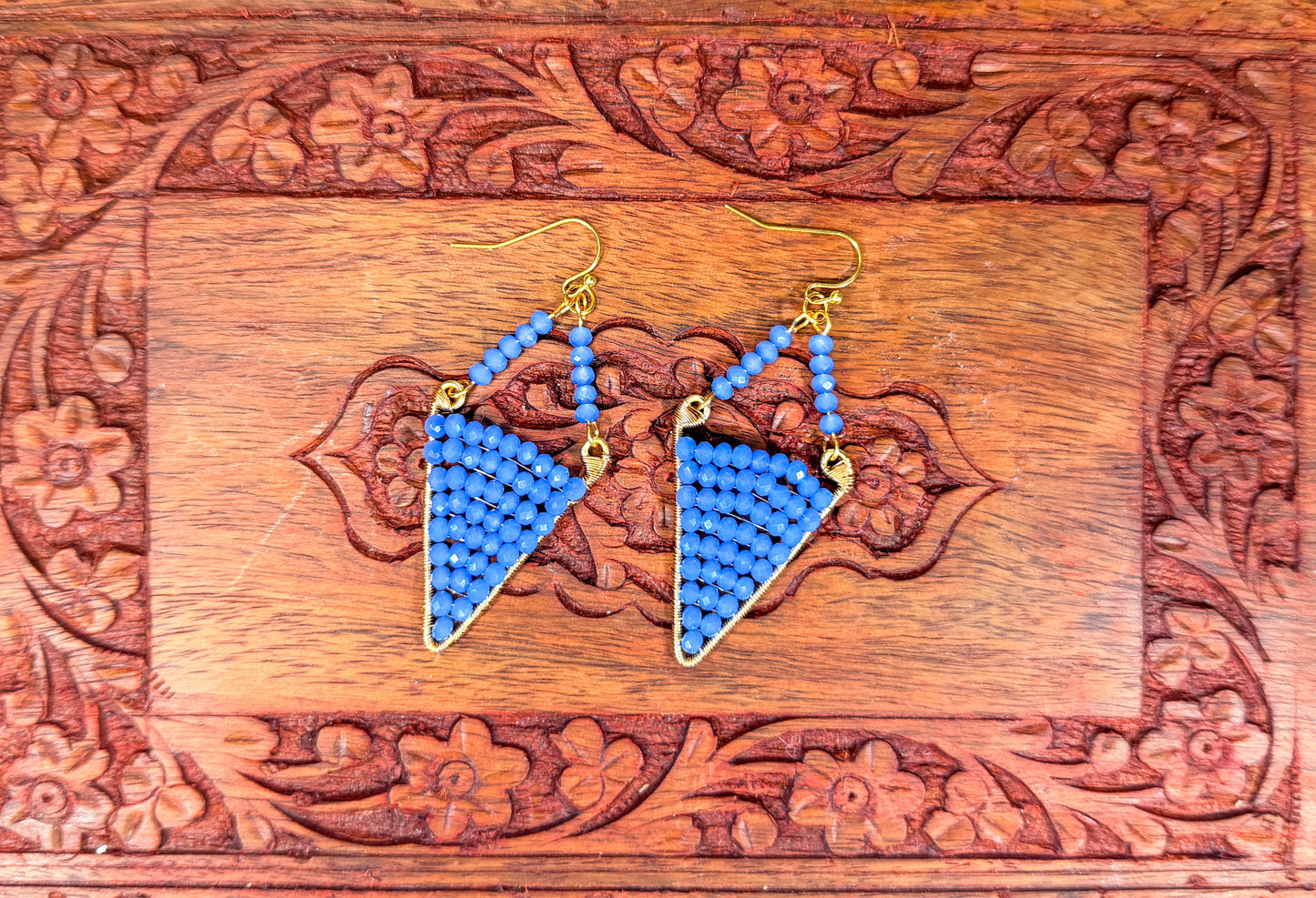Blue triangle-shaped earrings on a wooden box with floral patterns